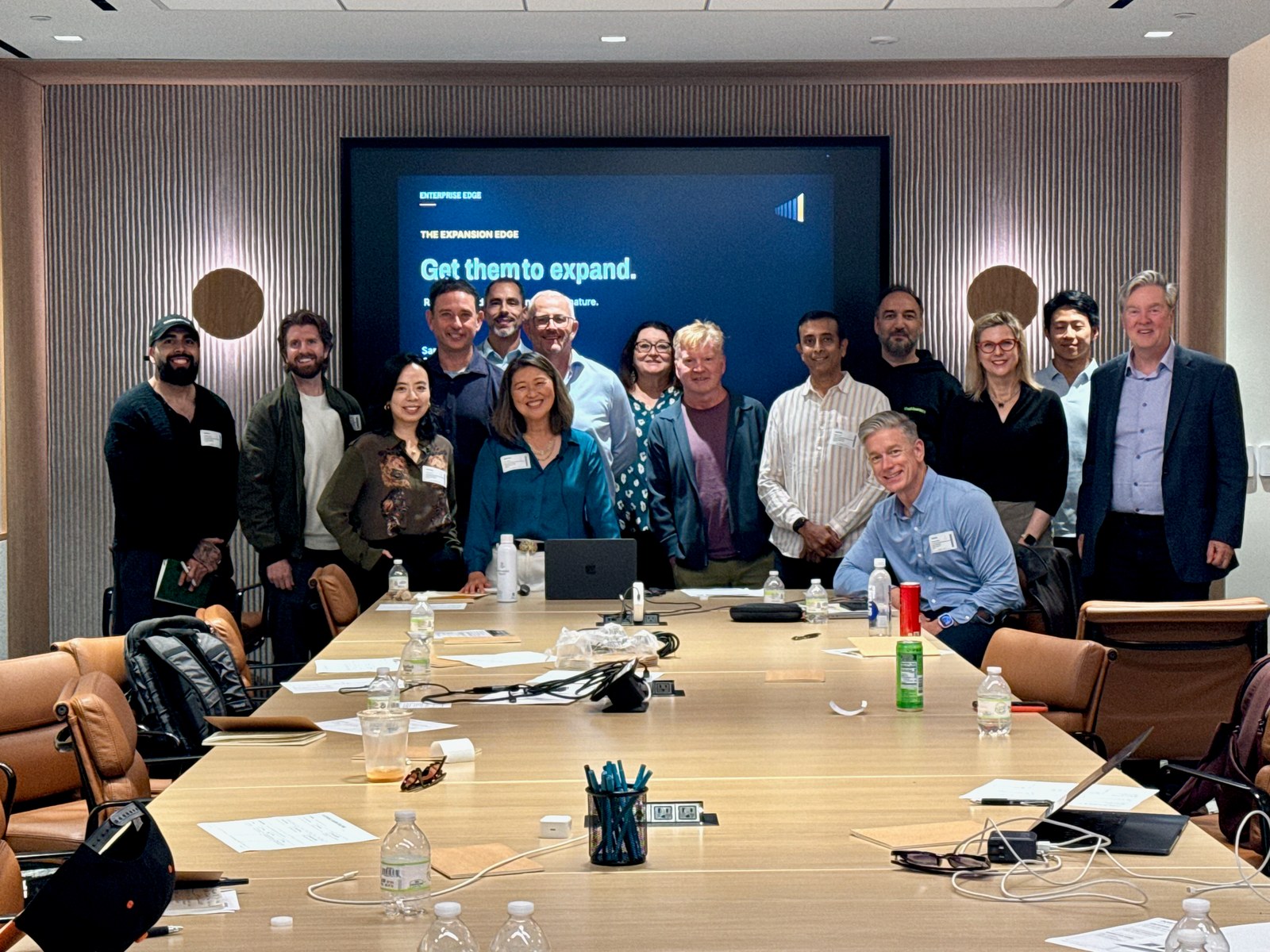 Workshop participants pose behind a conference table, with an Enterprise Edge presentation on screen.